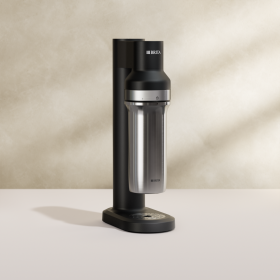 Der schwarze BRITA Wassersprudler sodaTRIO sprudelt Wasser auf vor einem beigefarbenen Hintergrund 